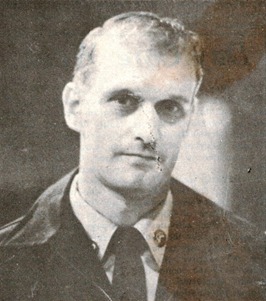 A grayscale portrait of a man in a suit and tie, with short hair, looking slightly to the side. The image has a vintage appearance.